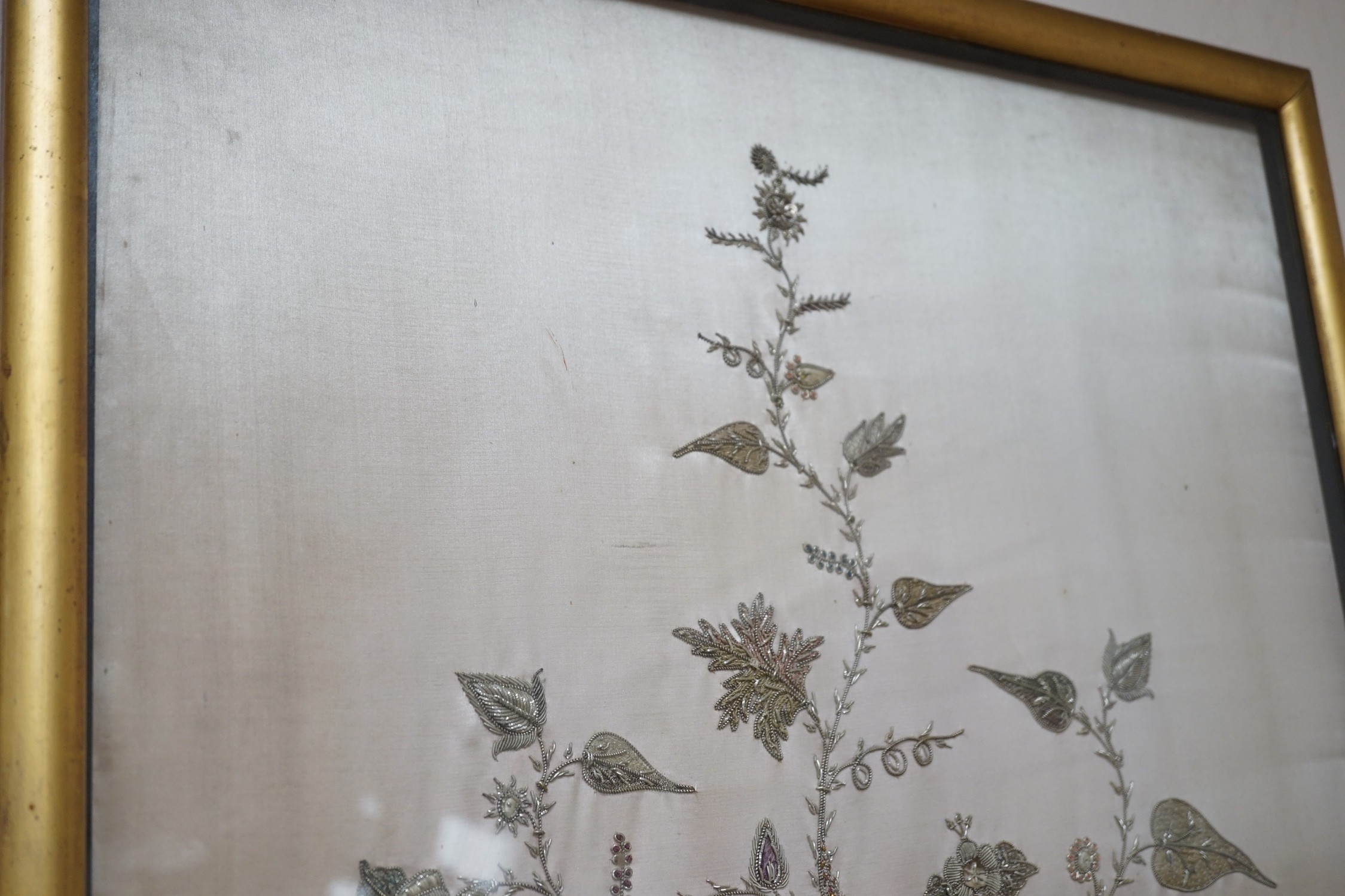 A framed silk, multi coloured metal thread embroidered Indian panel: a peacock seated amongst birds, flowers and leaves in a tree, 110cms x 51cms